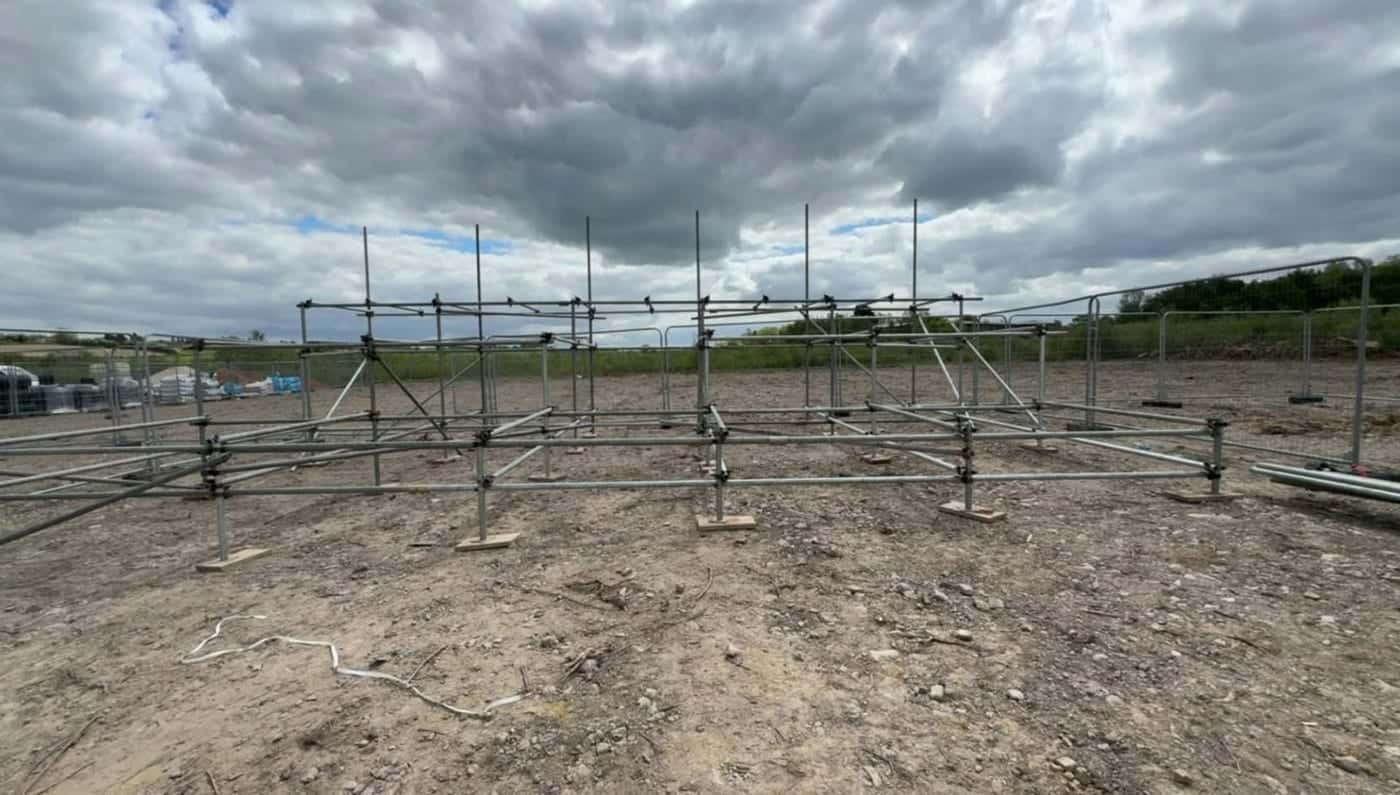 The base of a scaffold set out on sole boards across a cleared plot, standards up and the first ledgers on