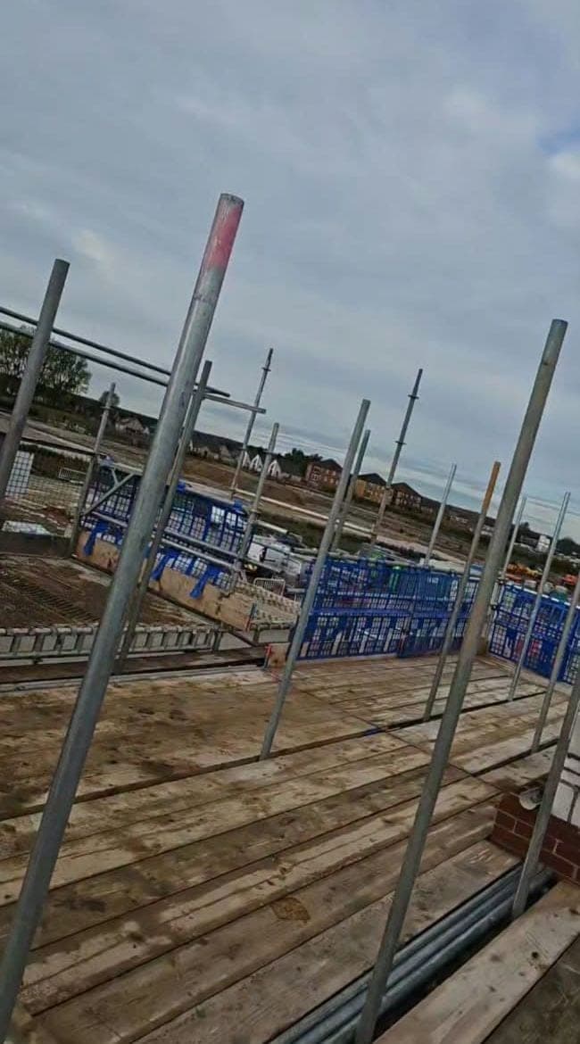 Looking along a boarded working lift, with standards and blue brick guards against a cloudy sky
