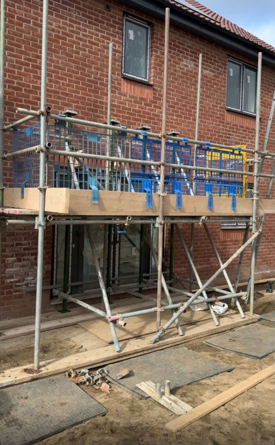 Boarded lift with toe boards and blue brick guards running along the rear of a new brick house